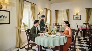 A dining area with a checkered floor, a round table with a green tablecloth, and chairs. - Tree of Life Sariska Manor (Rajgarh)