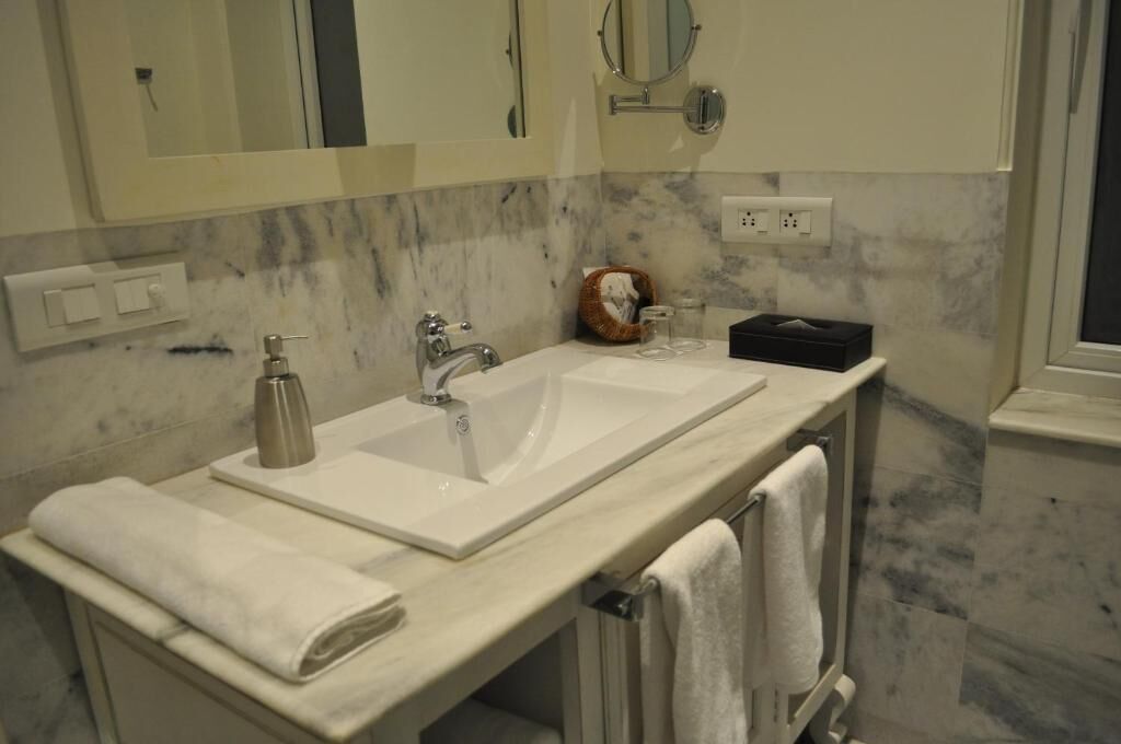 A bathroom with a large sink, two mirrors, a towel rack, and a marble backsplash.