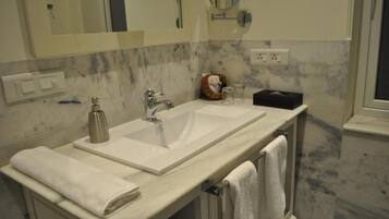 A bathroom with a large sink, two mirrors, a towel rack, and a marble backsplash.