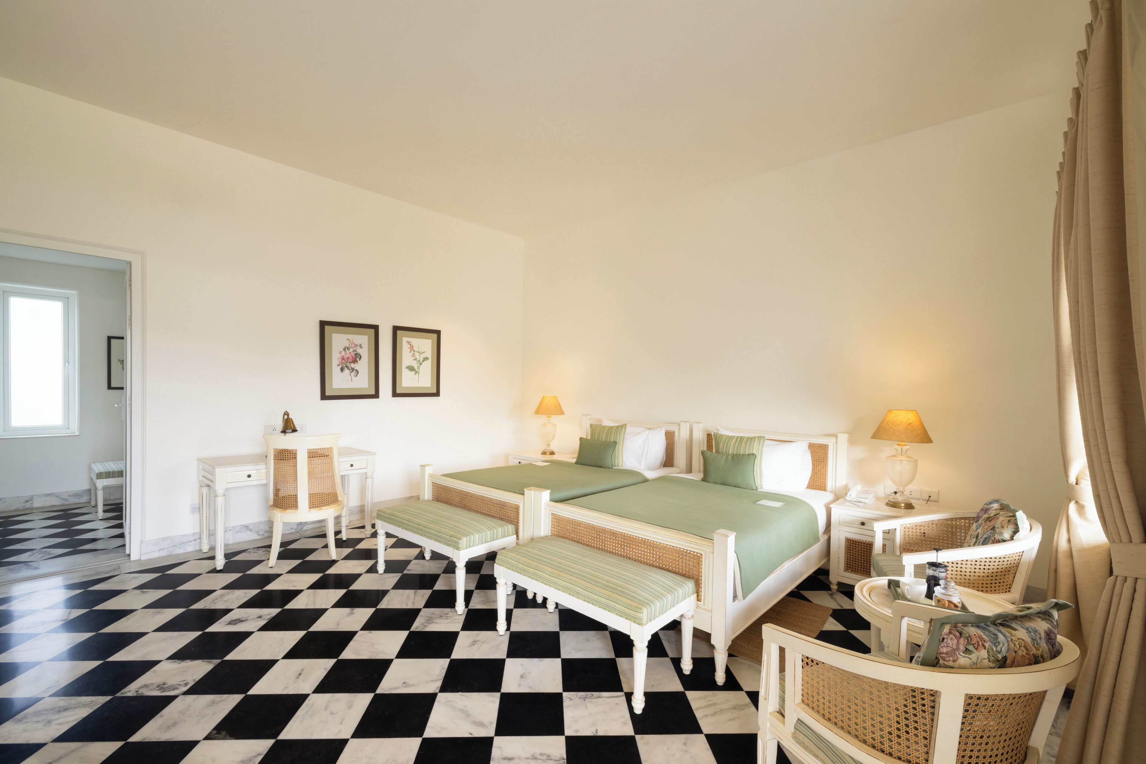 Una habitación de hotel con piso a cuadros, dos camas, un escritorio, una silla y una mesita de noche con lámpara.