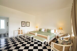 Una habitación de hotel con piso a cuadros, dos camas, un escritorio, una silla y una mesita de noche con lámpara.