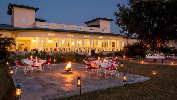 A building with a covered patio area, outdoor seating with tables and chairs, and a fire feature. - Tree of Life Sariska Manor (Rajgarh)