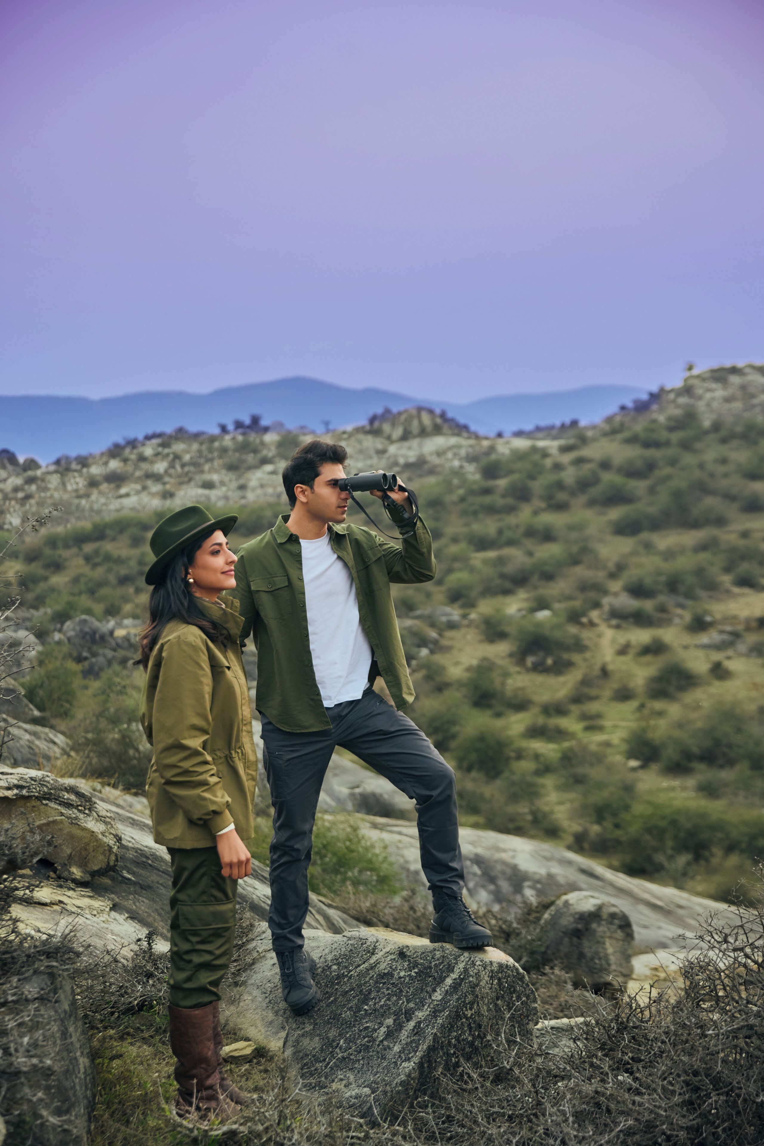 Una pareja parada sobre un saliente rocoso con montañas al fondo.