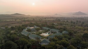 A residential area with multiple houses, a swimming pool, and a hilly landscape in the background. - Tree of Life Sariska Manor (Rajgarh)