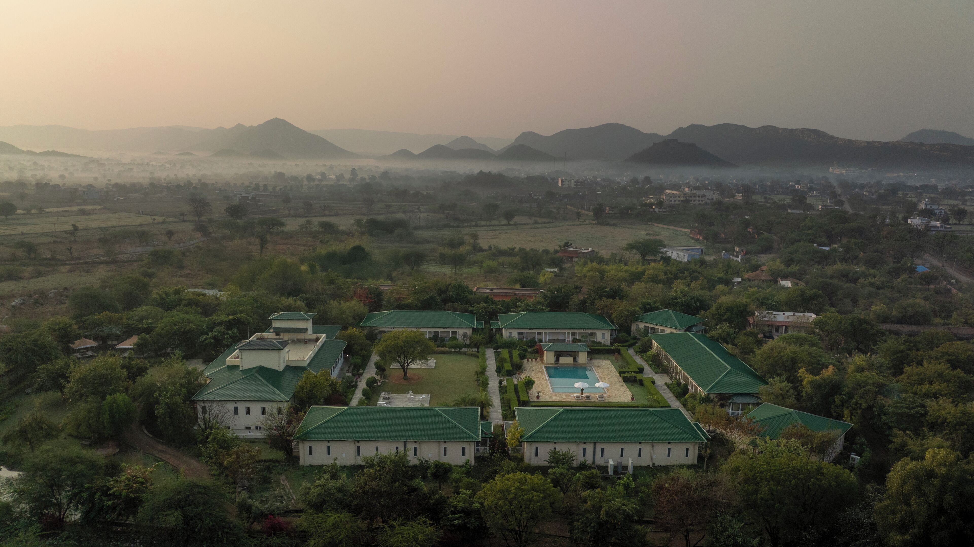 A residential area with multiple houses, a swimming pool, and a hilly landscape in the background.
