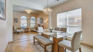 A dining area with a glass table, cushioned chairs, a bench, and a chandelier. - Arlington Home: Pool Oasis Near AT&T Stadium (Grand Prairie)