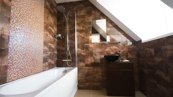 Un baño moderno con pared de mosaicos, una bañera independiente, cabina de ducha de vidrio y tocador de madera oscura.