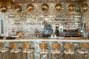 A bar area with a patterned wall, shelves with bottles, a coffee machine, and bar stools. - Small Premium Double with Balcony & Sea View (Newquay)