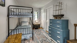 Een stapelbed met een bedsprei met dessin, een dressoir met lades, en een scheepsmodel erboven.