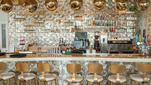Una zona de bar con mostrador, taburetes, estanterías llenas de botellas y una máquina de café.