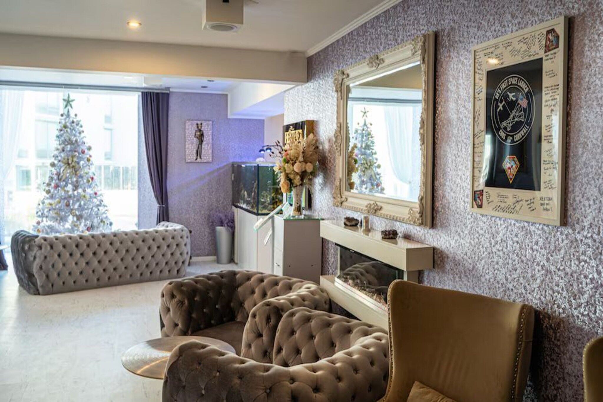 A living room with a large window, a fireplace, a Christmas tree, and a framed space shuttle logo.