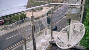 Un balcón con vista al litoral, una silla blanca y barandilla de vidrio.