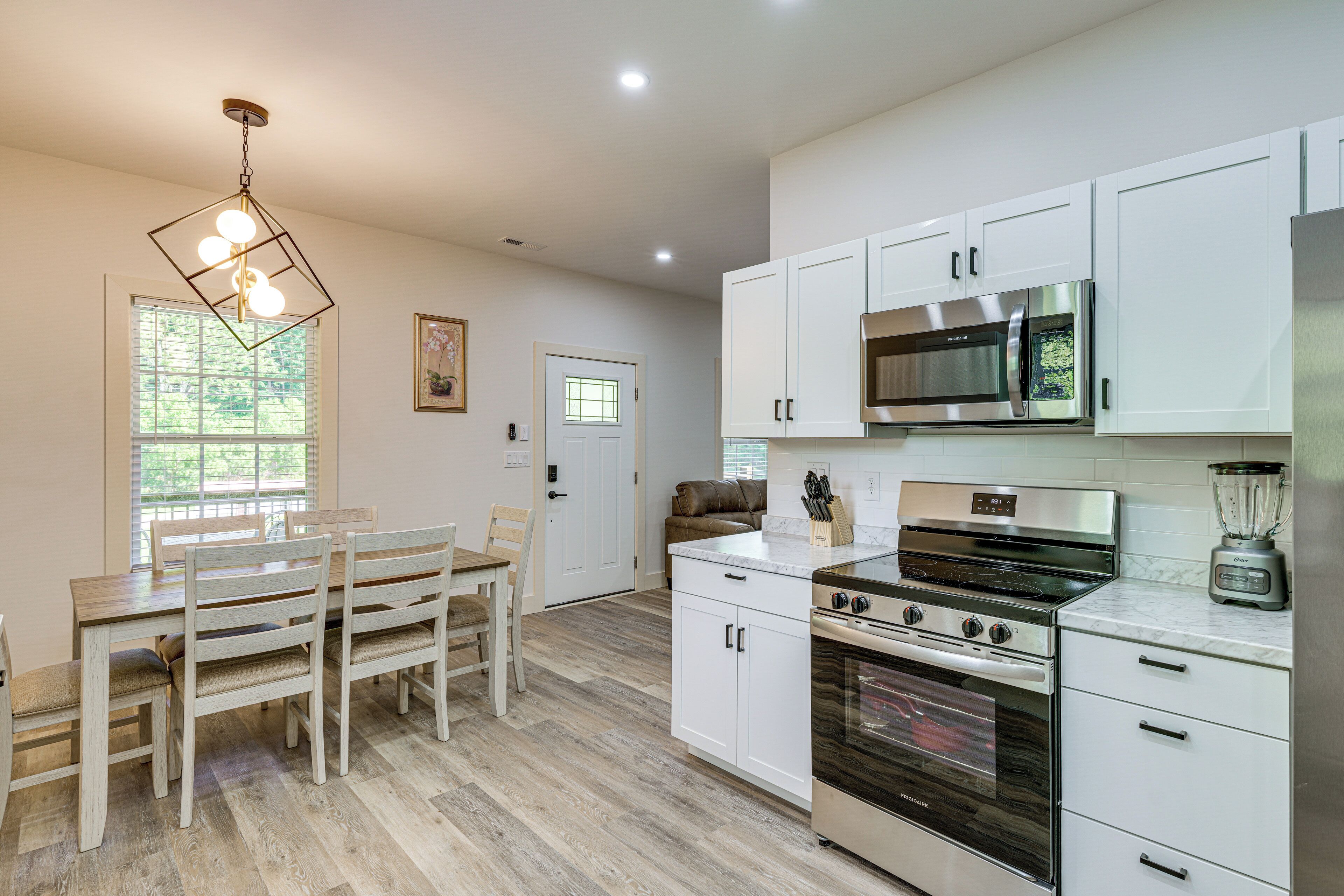 Una cocina moderna con armarios blancos, una estufa de acero inoxidable y un comedor con mesa y sillas de madera.