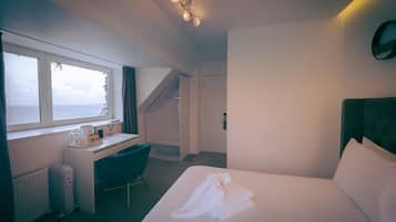 A hotel room with a bed, a desk, a chair, a radiator, and a window with a view.