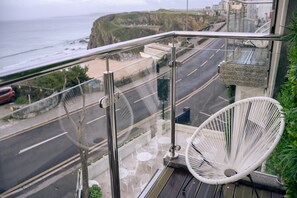 A balcony with a view of the coast, a white chair, and a glass railing. - Deluxe Double Room with View (Newquay)