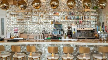 A bar area with a stone-patterned wall, multiple hanging light fixtures, a coffee machine, and bar stools.