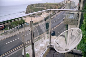 A balcony with a white chair, a view of a coastal road, and a glimpse of the ocean. - Newquay Beach by Sunday - Deluxe Double Room with View (Newquay)