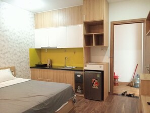 Ein kleiner Raum mit einem Bett, einer Küchenzeile, einem Kühlschrank und einer Tür zu einem weiteren Raum.