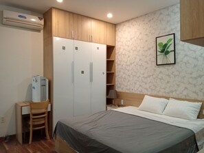 Ein Schlafzimmer mit einem Bett, einem Schreibtisch, einem Kleiderschrank und einer Wandpflanze.