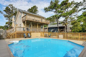 Una casa de dos pisos con piscina, terraza de madera y patio trasero cercado.