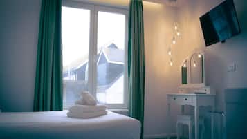 A hotel room with a bed, a desk, a mirror, and a TV on the wall.
