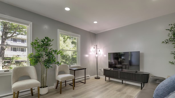 A modern living room with a large TV, two chairs, a small table, and a potted plant. - Modern Home Minutes to Mystic, Casinos and Ocean (Groton)