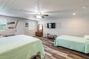 Une chambre avec deux lits, un ventilateur de plafond, une télévision et un plancher en bois.