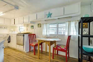 Une cuisine avec des meubles blancs, une cuisinière, une table avec des chaises et une fenêtre avec des rideaux.