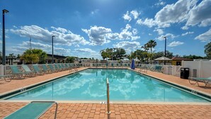 Una piscina rettangolare con bordo piastrellato, circondata da lettini e palme.