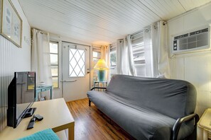 Une pièce avec un canapé, une table avec une lampe, un téléviseur et une fenêtre avec des rideaux.