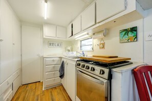 Une cuisine de taille réduite avec des meubles blancs, une cuisinière, une fenêtre et une pancarte indiquant « RELAX ».