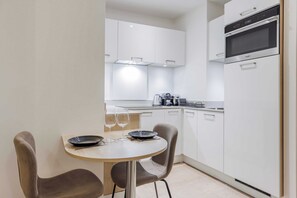 Uma cozinha moderna com armários brancos, forno embutido e área de jantar com duas cadeiras e uma mesa.