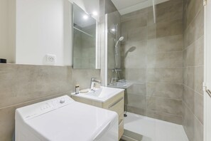 A modern bathroom with a built-in washing machine, a sink, and a shower. - Studio COSY - 2P - Boulogne Billancourt (Boulogne-Billancourt)