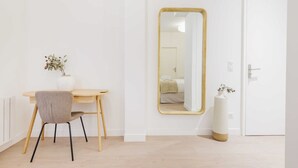 Ein schlicht eingerichteter Raum mit einem Holztisch, einem Stuhl, einem großen Spiegel und einer Tür.