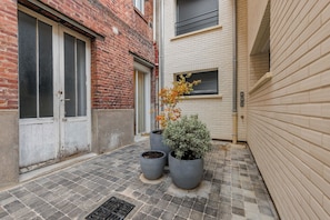 A narrow alleyway with a brick building, a white building with a window, and three potted plants. - Studio COSY - 2P - Boulogne Billancourt (Boulogne-Billancourt)