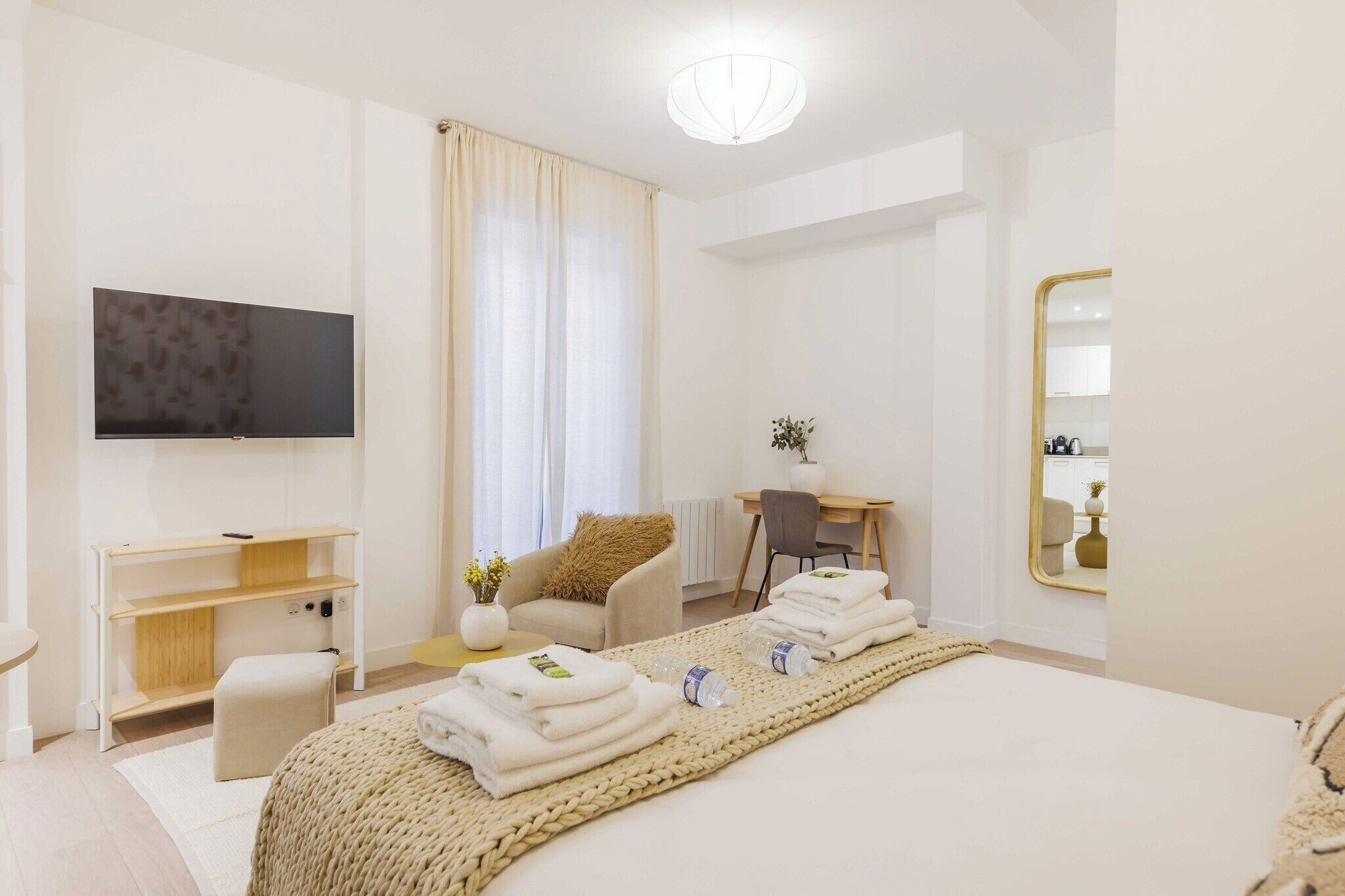 A modern hotel room with a large bed, a flat-screen TV, a desk, and a mirror.