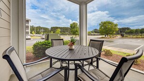 Eine überdachte Terrasse mit einem runden Tisch und vier Stühlen, einem Blumentopf und Blick auf einen Parkplatz und Bäume.