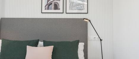 Una cama bien hecha con cabecera gris, almohadas verdes y blancas y una lámpara de noche negra.