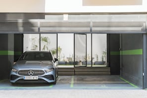 A car parked inside a covered parking area with a modern design, including a metal gate and a green stripe on the floor. - Edmond Vibes Madrid Río (Madrid)