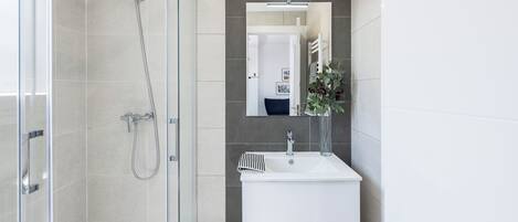 A modern bathroom with a glass shower enclosure, a white sink, and a mirror above it.