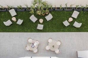 An outdoor seating area with lounge chairs and tables, surrounded by planters with various plants.