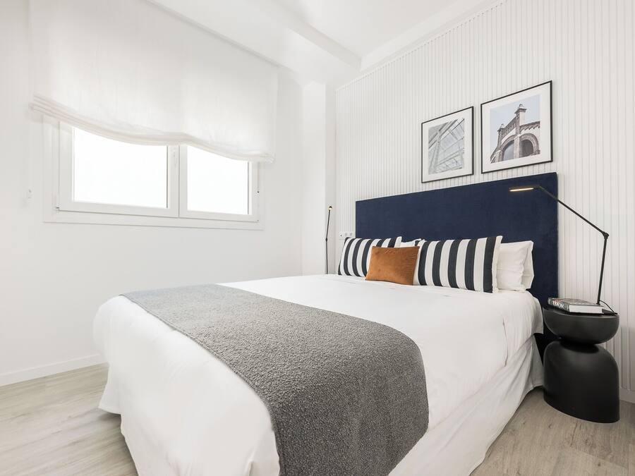 Een slaapkamer met een bed, nachtkastje, lamp en raam.