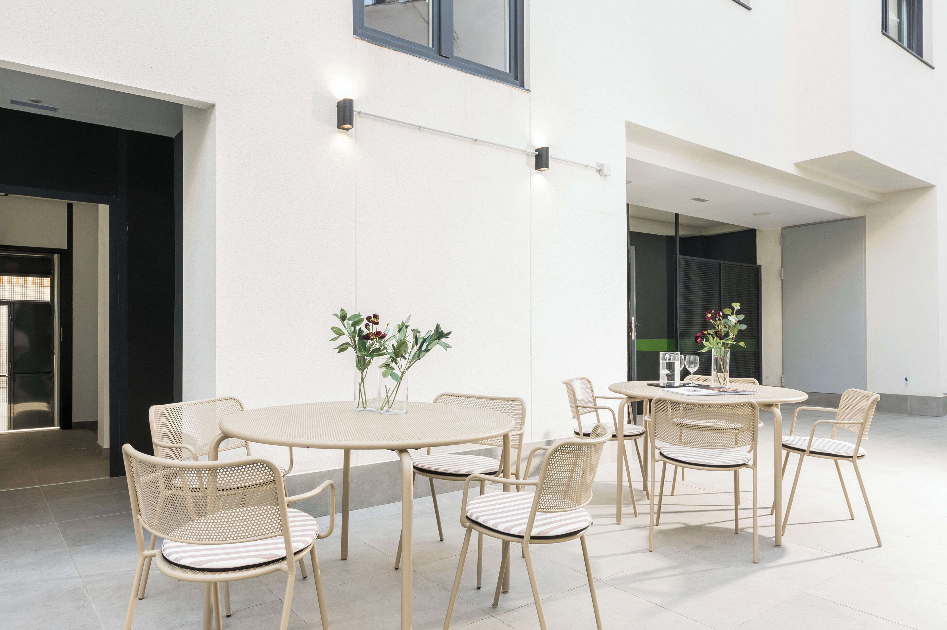 Un espace extérieur moderne aménagé avec des tables rondes et des chaises en osier, caractérisé par un design minimaliste et un mur extérieur blanc et épuré.