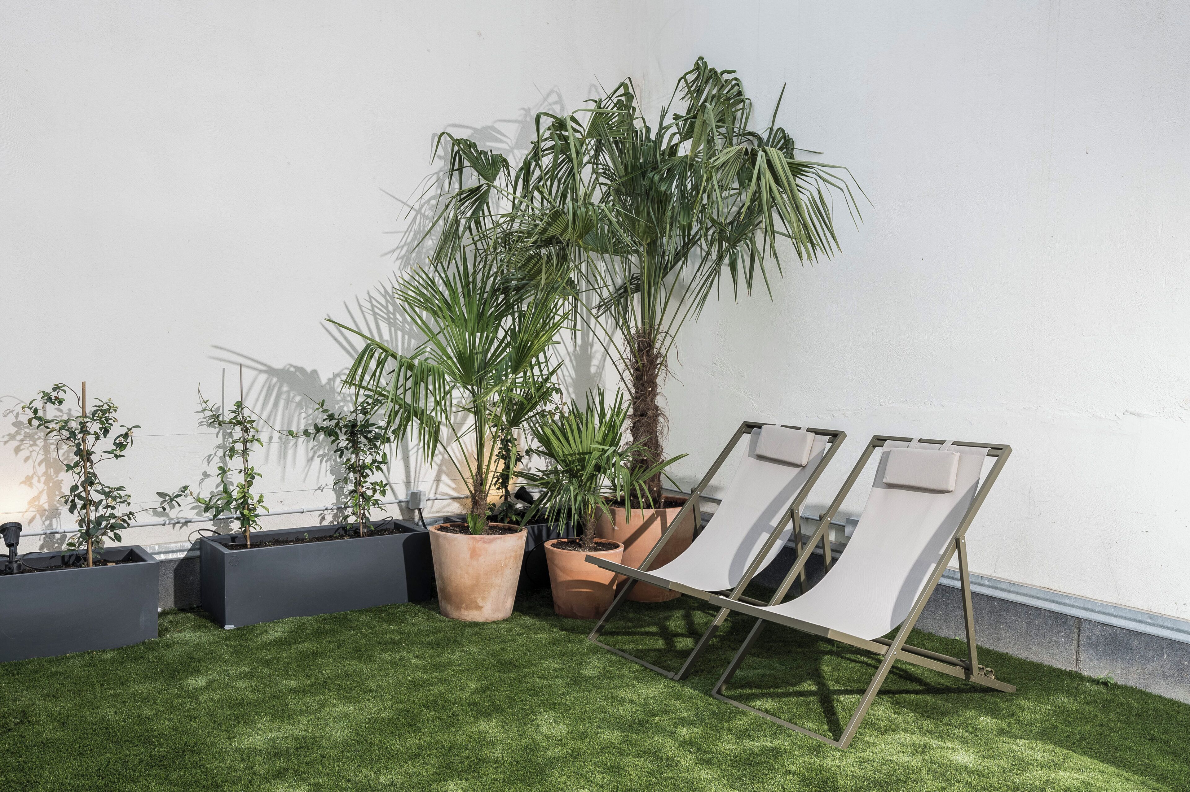 A garden area with various potted plants and a pair of white lounge chairs.