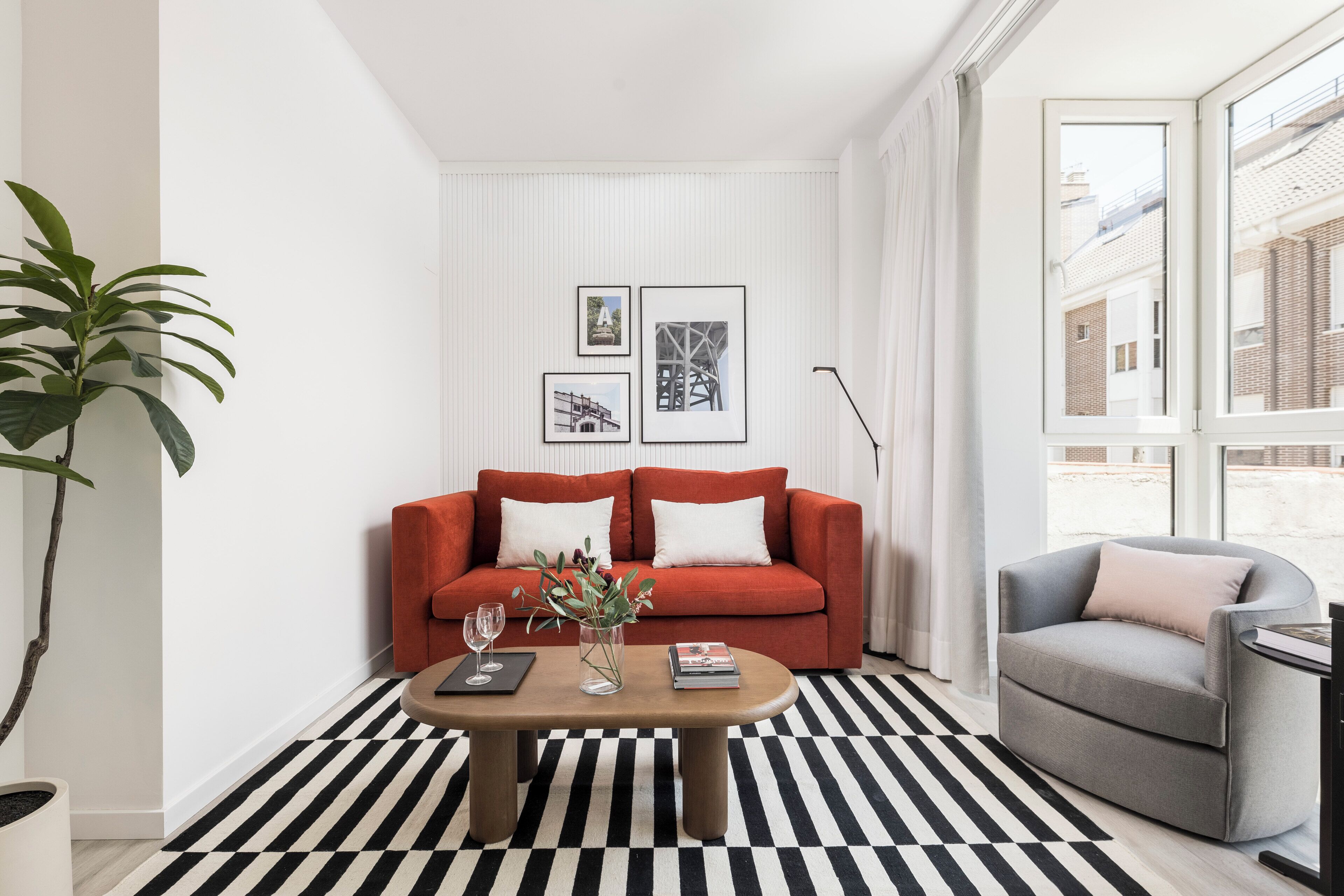 A modern living room with a red sofa, a grey armchair, a coffee table, and a black and white striped rug.