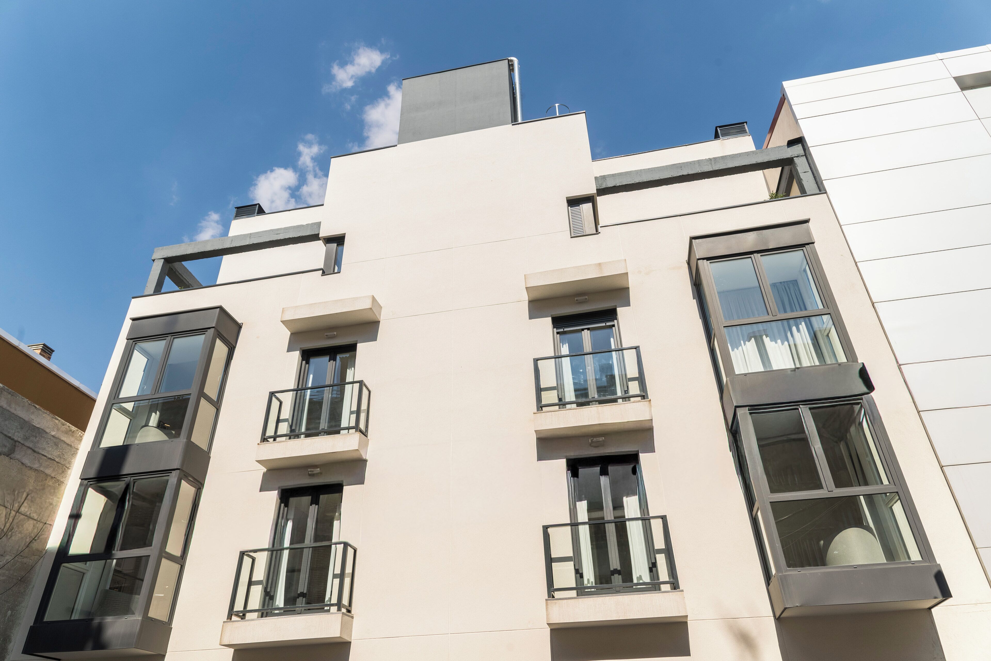 Un edificio moderno de varios pisos con balcones, ventanas grandes y techo plano.