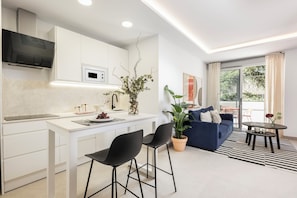 A modern kitchen with a white countertop, black chairs, a blue sofa, and a potted plant. - Edmond Vibes Torrespana (Madrid)