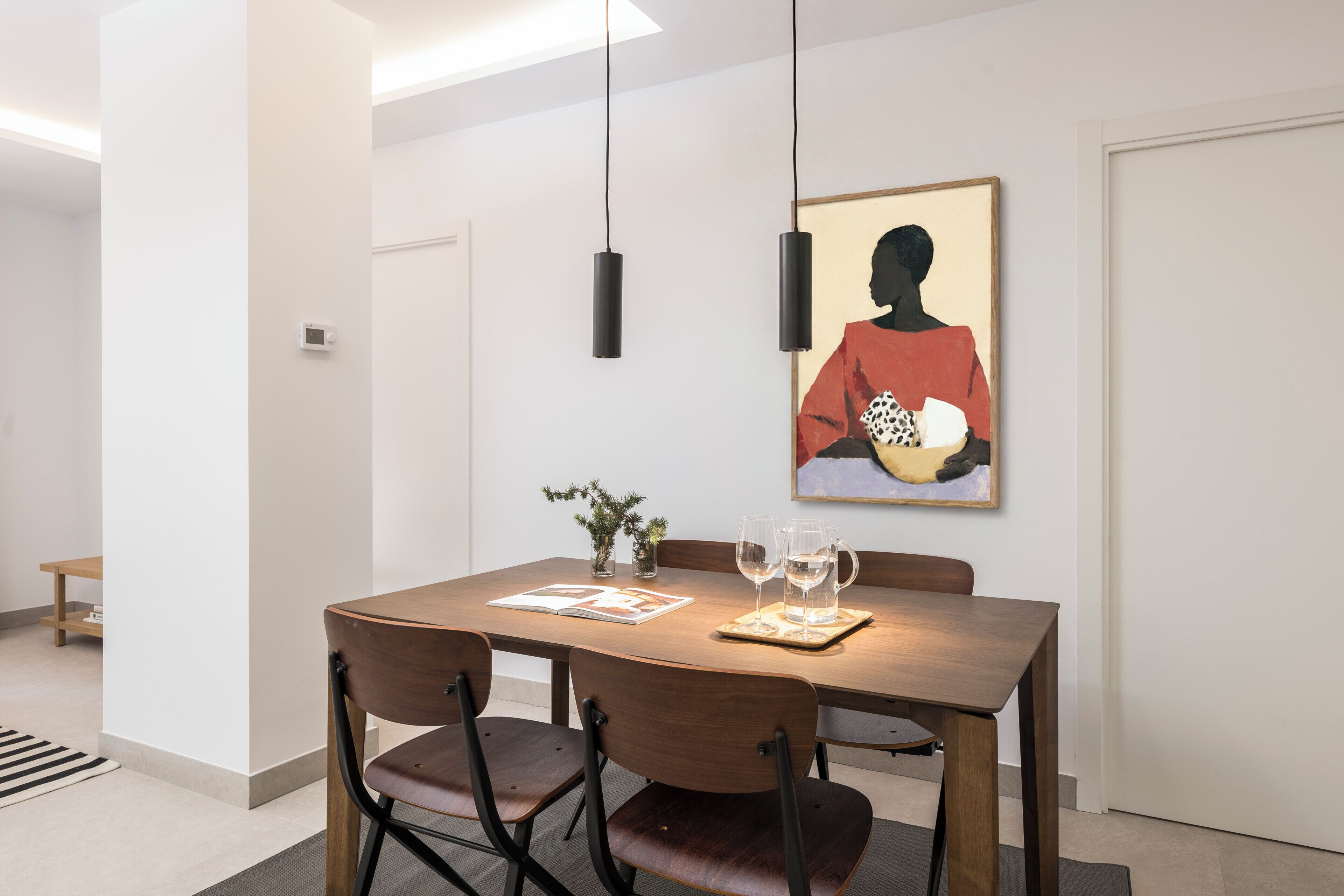 Een eetgedeelte met een houten tafel, vier stoelen, twee wijnglazen en een kunstwerk in een lijst aan de muur.