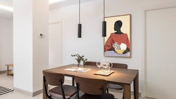Een eetgedeelte met een houten tafel, vier stoelen, twee wijnglazen en een kunstwerk in een lijst aan de muur.