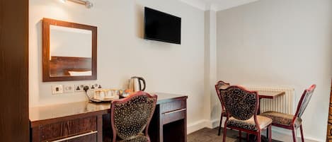 Habitación de hotel con un escritorio de madera, dos sillones tapizados, un televisor de pantalla plana y un espejo en la pared.